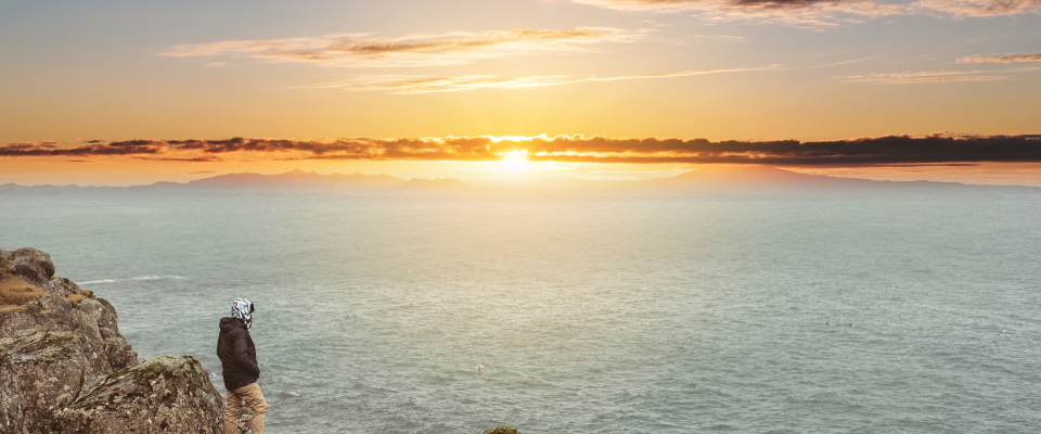 Ein Mann steht während des Sonnenuntergangs an einer Klippe. (Symbolbild)