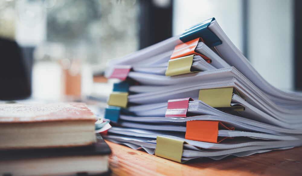 Ein Stapel von Dokumenten, der auf dem Schreibtisch liegt und darauf wartet überprüft zu werden. (Symbolbild)